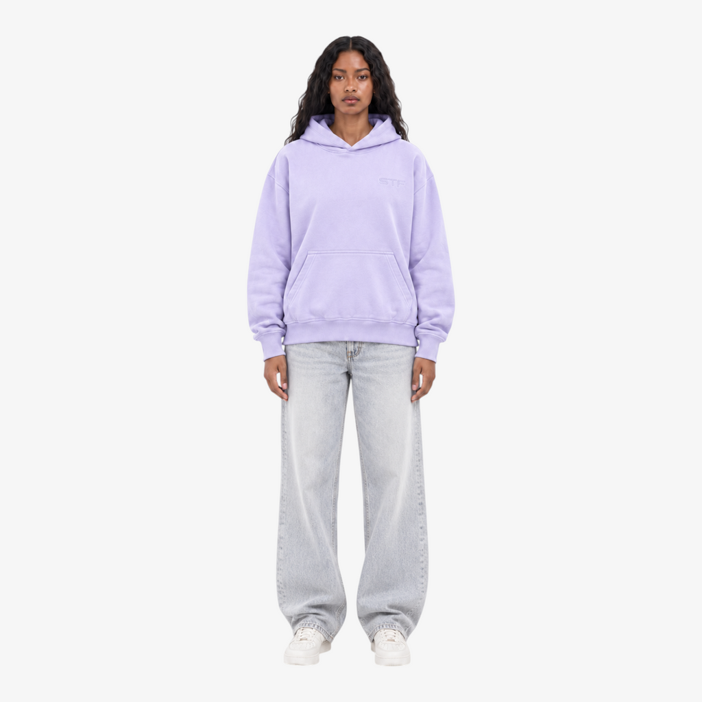 Model wearing a Seejthreadsflames (STF) lavender pullover hoodie with chest embroidery, paired with light wash jeans.
