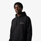 Model wearing a Seejthreadsflames (STF) black heavyweight cotton pullover hoodie with chest embroidery